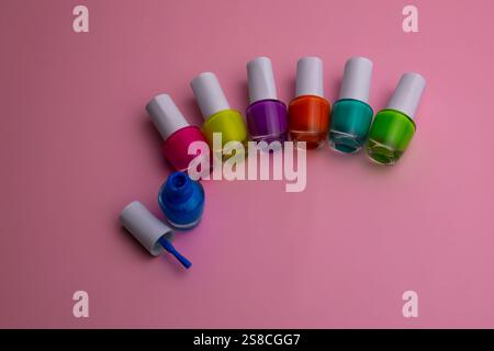 Questa immagine mostra una collezione di colorate bottiglie di smalto disposte in forma semicircolare su sfondo rosa. I flaconi presentano una varietà Foto Stock