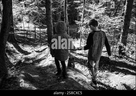 Due bambini, un fratello e una sorella, camminano mano nella mano lungo un sentiero sterrato in una foresta baciata dal sole. Stanno godendo di una tranquilla avventura all'aria aperta. Foto Stock