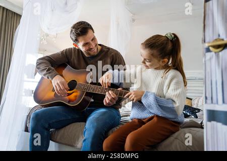 Felice padre single che insegna a sua figlia, figlio, a suonare la chitarra a casa. Foto Stock