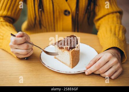 Una persona in un intimo maglione giallo si gode una fetta di torta ricoperta di cioccolato, avvolta da una forchetta, la scena trasuda calore e deliziosa indulgenza Foto Stock