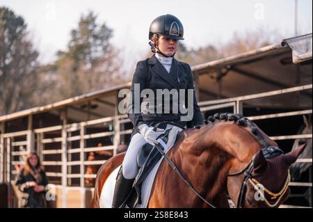Una teenager incentrata gareggia in un evento di dressage classico, vestito con abiti tradizionali, cavalcando un cavallo ben curato. Foto Stock
