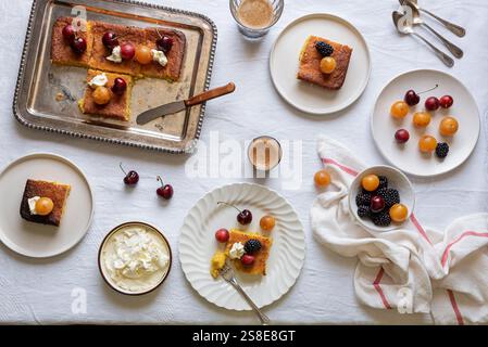 Vista dall'alto di un dolce tavolo da dessert con fette di torta impreziosite da ciliegie, more e panna montata, accompagnate da tazze di caffè. Foto Stock