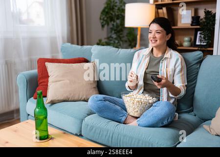 Giovane felice appena divorziata o donna single di recente dopo la rottura della relazione tossica seduta da sola a casa sul divano, mangiando popcorn e guardando movi Foto Stock
