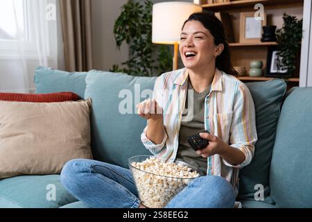 Giovane felice appena divorziata o donna single di recente dopo la rottura della relazione tossica seduta da sola a casa sul divano, mangiando popcorn e guardando movi Foto Stock