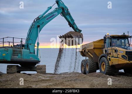 Eastbourne, East Sussex, Regno Unito - 13 gennaio 2025 - un escavatore che carica un camion con trampolino sulla spiaggia. Questa immagine evidenzia l'ef Foto Stock