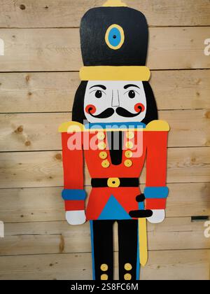 La colorata figura dello schiaccianoci in legno si erge contro una parete di legno in un ambiente festoso durante le vacanze invernali Foto Stock