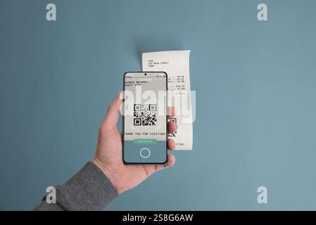 Smartphone che esegue la scansione di un codice QR su una ricevuta cartacea posizionata su un tavolo, illustrando il concetto di pagamento digitale delle bollette utilizzando la tecnologia mobile Foto Stock