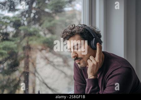 Giovane e affascinante uomo dall'aspetto mediorientale con cuffie sovraurali che ascoltano musica e si rilassano. Foto Stock