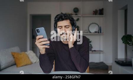 Giovane e affascinante uomo dall'aspetto mediorientale con cuffie sovraurali che ascoltano musica e si rilassano. Foto Stock