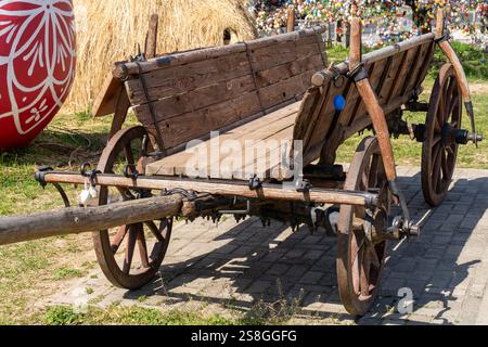 Un carrello in legno d'epoca esposto all'aperto, caratterizzato da dettagli rustici e circondato da decorazioni natalizie pasquali, tra cui un grande uovo dipinto. Foto Stock