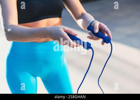 Una donna ha due corde in mano. Indossa pantaloni blu e un top nero Foto Stock