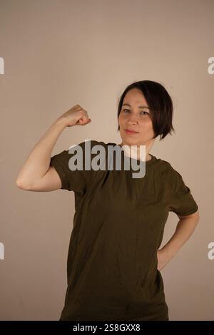 Ritratto di una bella, attraente bruna matura. Donna con t-shirt casual che mostra bicipiti isolati sullo sfondo dello studio. Sport e assistenza sanitaria Foto Stock