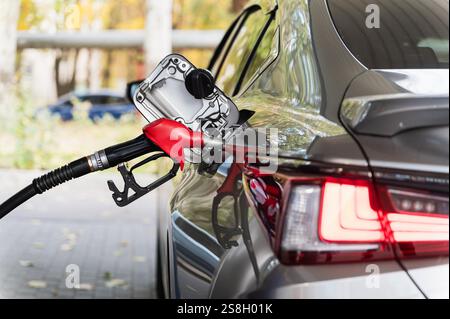 Un'auto sta facendo rifornimento in un distributore di benzina. Primo piano dell'ugello del carburante inserito nel serbatoio del carburante dell'auto. Vista dalla parte posteriore. Foto Stock