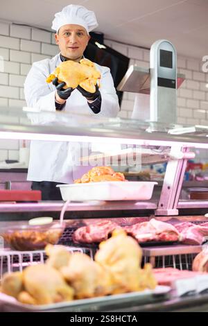 Macellaio maschile che mostra pollo intero fresco in macelleria Foto Stock