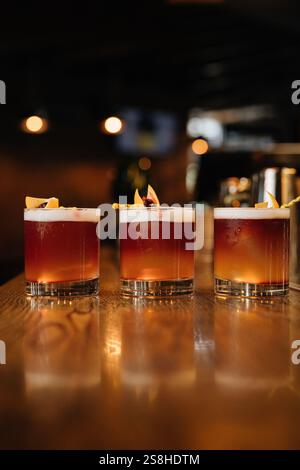 Tre vivaci cocktail su un bancone bar in legno, perfetto per la vita notturna e temi di mixology Foto Stock