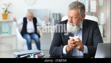 Uomo maturo arrabbiato che sfrega la carta in ufficio durante la lite con il collega Foto Stock