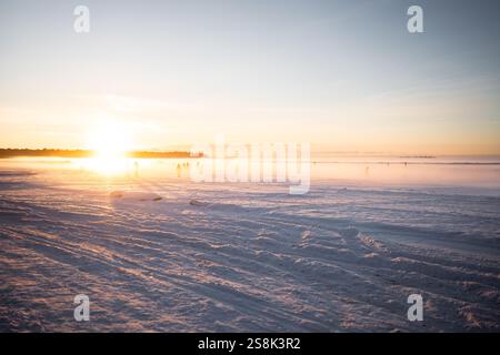 Gruppi che passeggiano sul ghiaccio e sulla baia innevata con il tempo freddo alla luce del tramonto. Lago ghiacciato Foto Stock