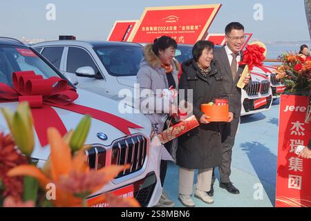 YANTAI, CINA - 23 GENNAIO 2025 - i dipendenti vincitori scattano una foto con le loro famiglie accanto all'auto premiata durante la cerimonia di premiazione di Jierui Gro Foto Stock