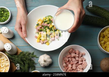 Preparare la zuppa di okroshka. Donna che versa kefir nella ciotola con ingredienti diversi sul tavolo di legno azzurro, vista dall'alto Foto Stock Preparare la zuppa di okroshka. Donna che versa kefir nella ciotola con ingredienti diversi sul tavolo di legno azzurro, vista dall'alto Foto Stock