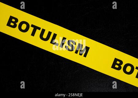 Concetto di attenzione, pericolo e avvertenza per avvelenamento da cibo botulismo. Nastro da barricata giallo con scritta su sfondo nero scuro. Foto Stock