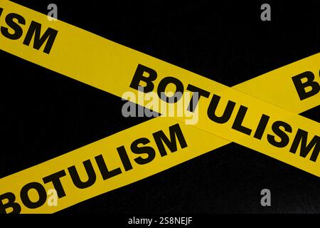 Concetto di attenzione, pericolo e avvertenza per avvelenamento da cibo botulismo. Nastro da barricata giallo con scritta su sfondo nero scuro. Foto Stock