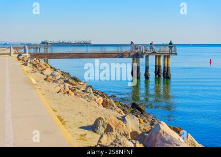 Long Beach, California - 15 gennaio 2025: Vista di un molo di legno che si estende sulle acque calme di Long Beach, con persone che si godono il lungomare mentre s Foto Stock