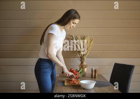 Donna che taglia pomodori freschi per insalata in cucina con pareti in legno Foto Stock