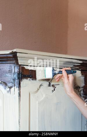 Artigiano che applica vernice di gesso bianco su mobili in legno antico utilizzando pennelli, ristrutturazioni domestiche e concetto di restauro di mobili Foto Stock