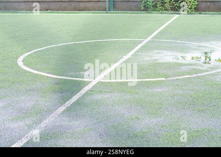 Vista ravvicinata di un campo da calcio con una tacca centrale circolare. Il tappeto erboso artificiale è bagnato, mostrando macchie d'acqua sulla superficie. L'ar circostante Foto Stock