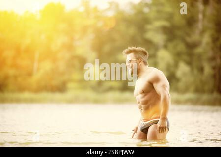 Immagine di un uomo muscoloso nel lago con camicia bianca e occhiali da sole Foto Stock