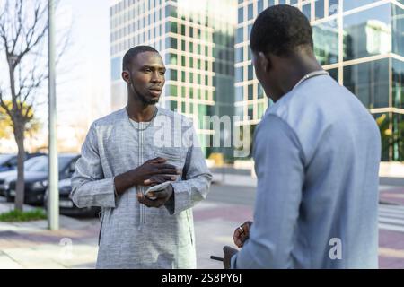Due uomini d'affari senegalesi in abito dashiki stanno facendo una conversazione all'aperto, potenzialmente discutendo di un accordo d'affari Foto Stock