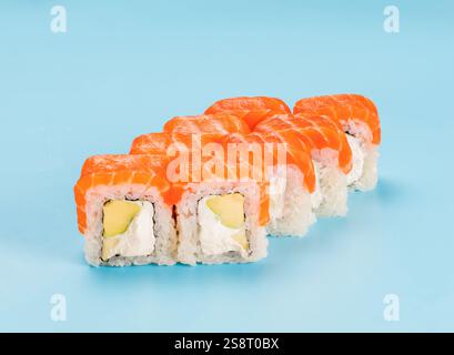 Fotografia in studio di Philadelphia Roll di vellutato formaggio spalmabile e avocado, avvolti in un perfetto sushi di riso stagionato e salmone fresco. Isolato su sfondo blu chiaro fisso Foto Stock