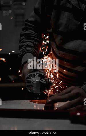Scintille di saldatura che volano dal metallo mentre l'operatore fonde l'acciaio con una fiamma blu intensa, creando fumo e particelle luminose durante il processo di fabbricazione Foto Stock