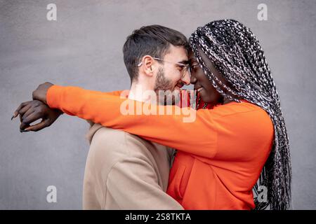 Una coppia interrazziale gioiosa che condivide un abbraccio amorevole in uno sfondo neutrale, simboleggiando l'amore, la diversità e la solidarietà in un'atmosfera vibrante e sentita Foto Stock
