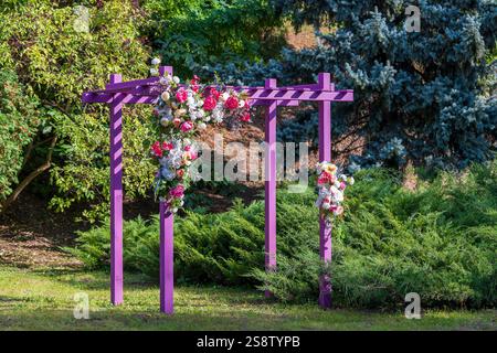 Vista frontale di un pergolato rosa decorativo con fiori artificiali nel giardino urbano, primo piano Foto Stock