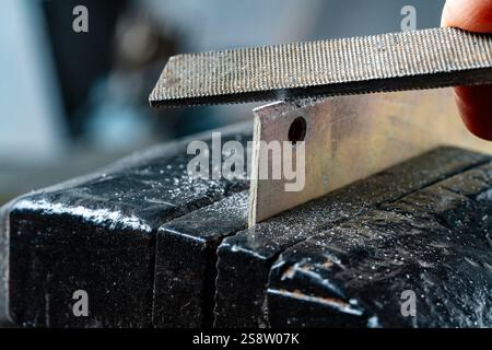 L'artigiano lavora su un piccolo pezzo di metallo con lima metallica presa in morsa sul tavolo del banco di lavoro in officina, concetto fai da te, primo piano Foto Stock