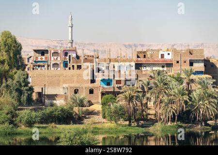 Una tranquilla cittadina lungo il fiume di Naqadah in Egitto, con edifici tradizionali e vegetazione lussureggiante, con deserto del Sahara alle spalle Foto Stock