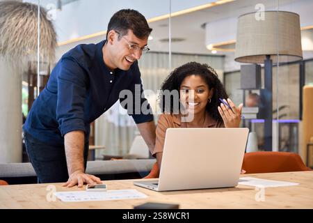 Due giovani e eterogenei colleghi di lavoro che utilizzano un notebook in un ufficio moderno. Foto Stock