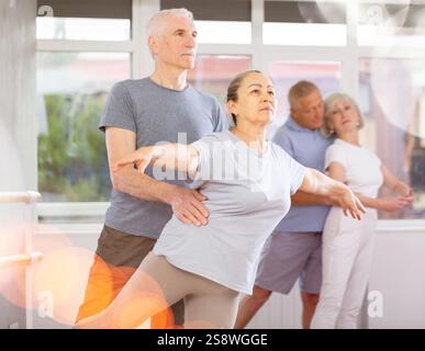 Ballerina donna matura e vecchio partner maschio che praticano la posa arabesca di balletto durante l'allenamento con persone attive di gruppo in studio di coreografia Foto Stock