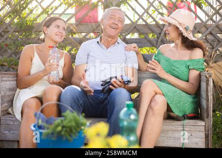 Un uomo e due donne che parlano sulla panchina da giardino Foto Stock