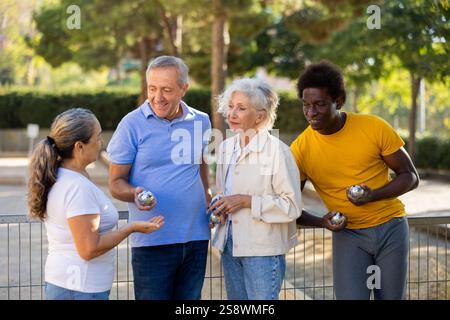Amici maturi e polirazziali sorridenti mentre tengono le palle di petanque in metallo all'aperto Foto Stock
