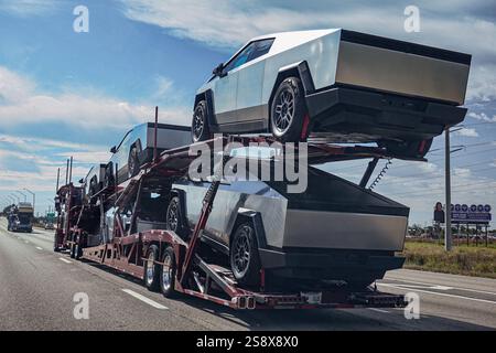 Miami, Stati Uniti - 20 gennaio 2025: Il trasportatore di auto trasporta nuovi veicoli Tesla cybertrck lungo l'autostrada, vista posteriore del rimorchio. Foto Stock