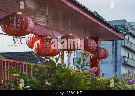 Una fila di lanterne rosse cinesi appese sotto un tetto, con vista su una città sullo sfondo. Queste lanterne sono spesso usate come decorazioni durante Chine Foto Stock