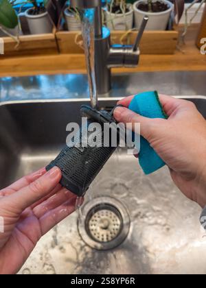Pulizia delle mani di un filtro per lavastoviglie con spugna blu nel lavello della cucina . Foto di alta qualità Foto Stock