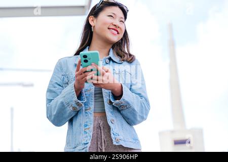 Sorridente giovane donna che tiene in mano smartphone in ambiente urbano Foto Stock