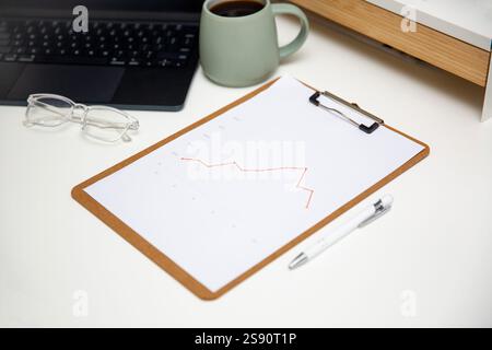 Tavolo da lavoro per ufficio con grafici, report su appunti in legno, caffè, forniture e laptop. Foto Stock