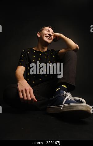 Un giovane allegro che posa abiti alla moda su uno sfondo scuro Foto Stock
