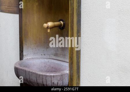 Un vecchio rubinetto montato a parete con un bacino in pietra da cui gocciola l'acqua. Foto Stock