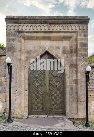 La splendida porta presenta dettagliate incisioni geometriche all'interno di un arco in pietra splendidamente lavorato. Due lampioni ornamentali incorniciano l'ingresso, migliorando il fascino architettonico Foto Stock