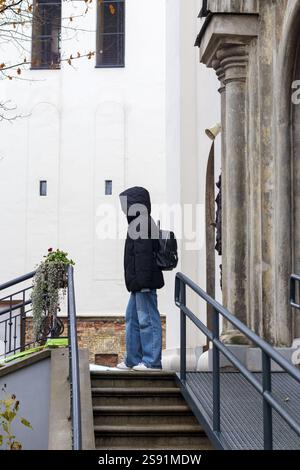 Un uomo con uno zaino in piedi sui gradini di un edificio situato nella città vecchia. Foto Stock